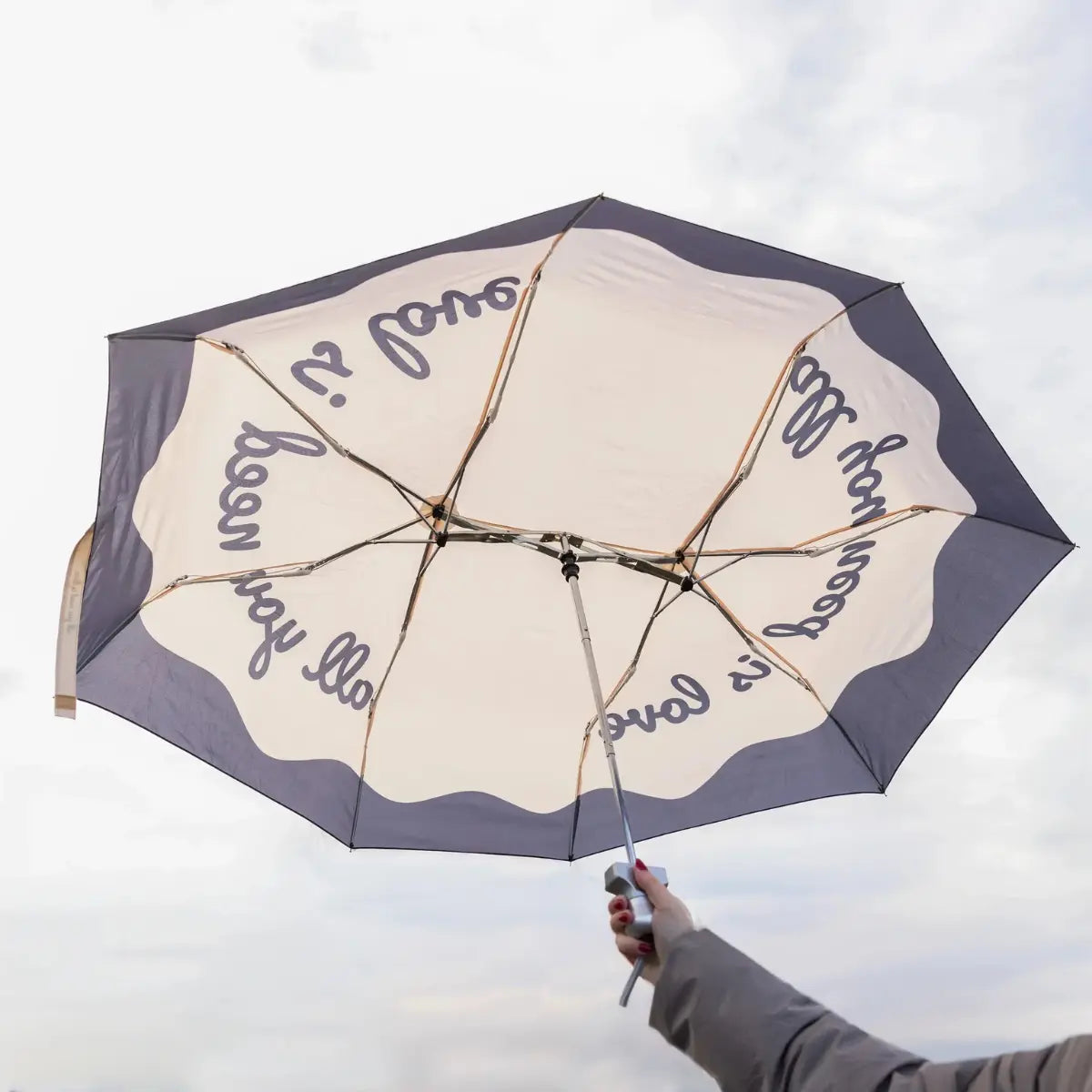 Ombrello tascabile doppio all you need is love tenuto in mano da una donna. Sfondo cielo grigio