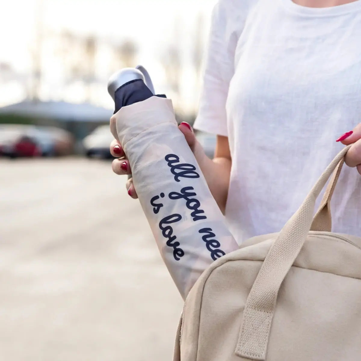 Mano femminile che infila l'ombrello richiuso all you need is love nello zaino color crema