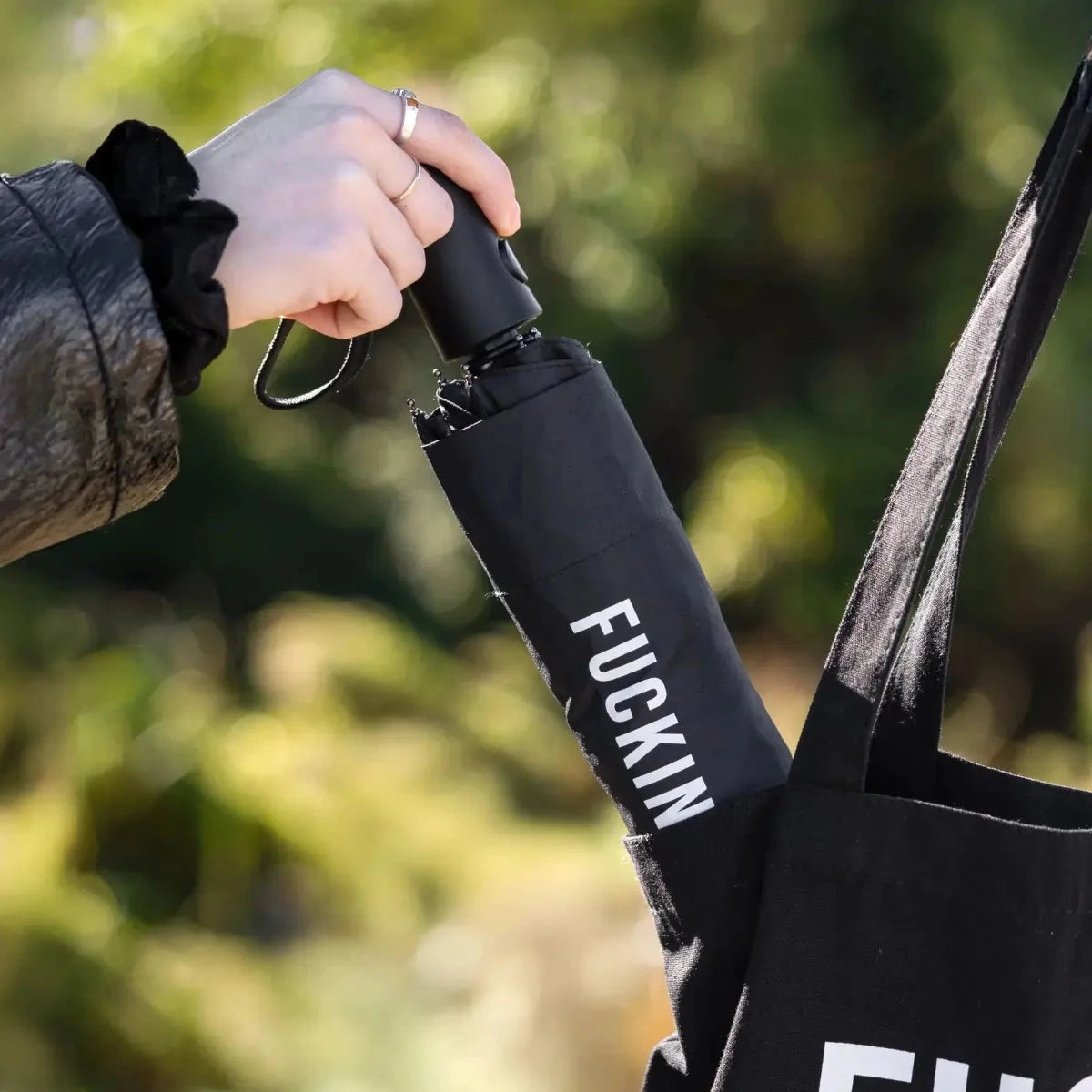 Mano che mette l'ombrello fucking rain nero chiuso dentro una borsa nera. Sfondo giardino