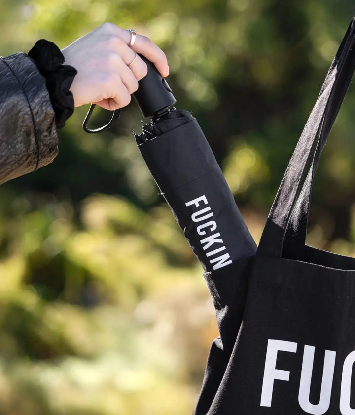 Mano che mette l'ombrello fucking rain nero chiuso dentro una borsa nera. Sfondo giardino