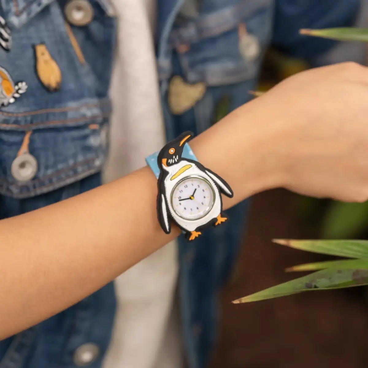 Polso di un bambino che indossa orologio con pinguino bianco e nero con cinturino azzurro 