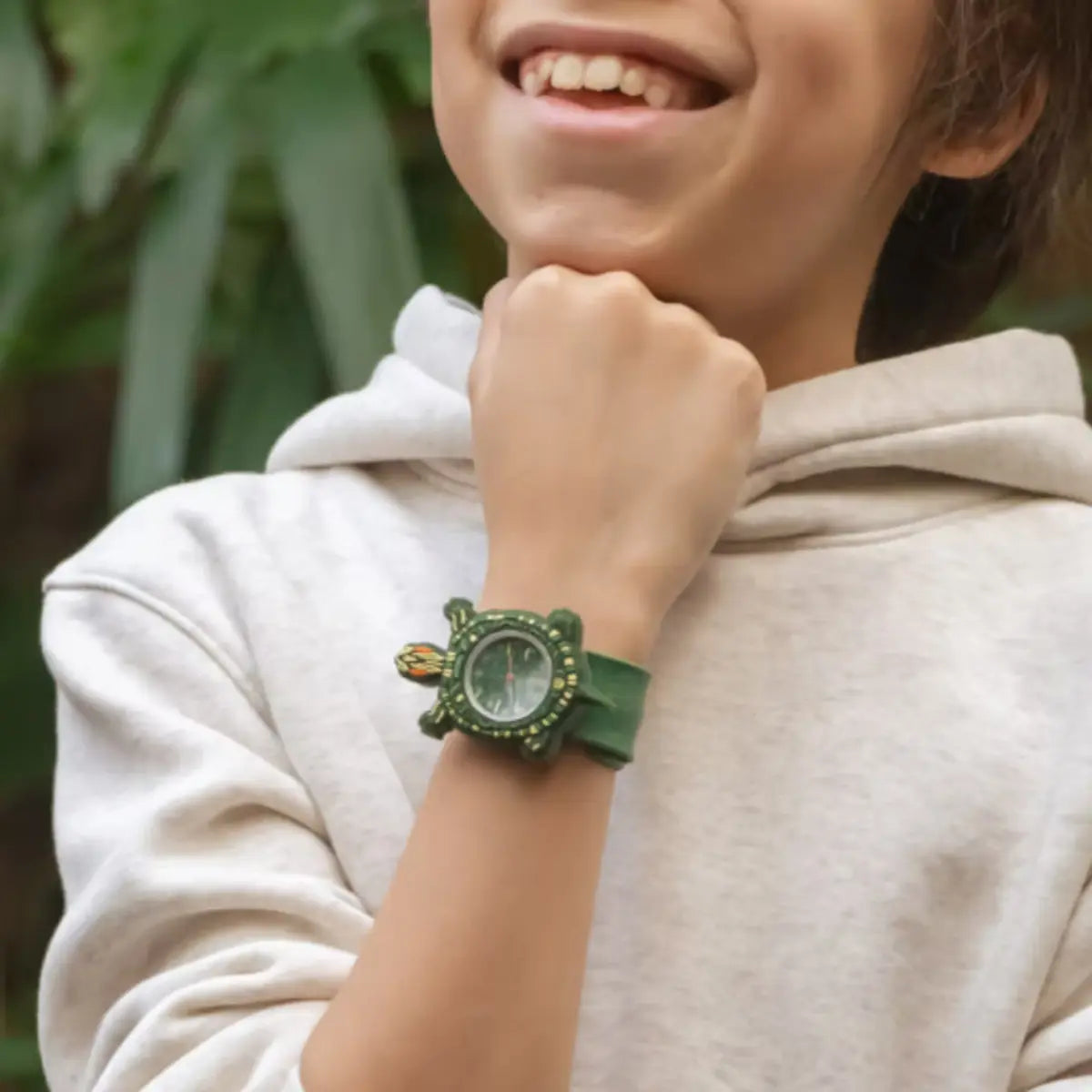 Bambino che sorride con braccio appoggiato al mento. Al polso ha un orologio verde con una tartaruga