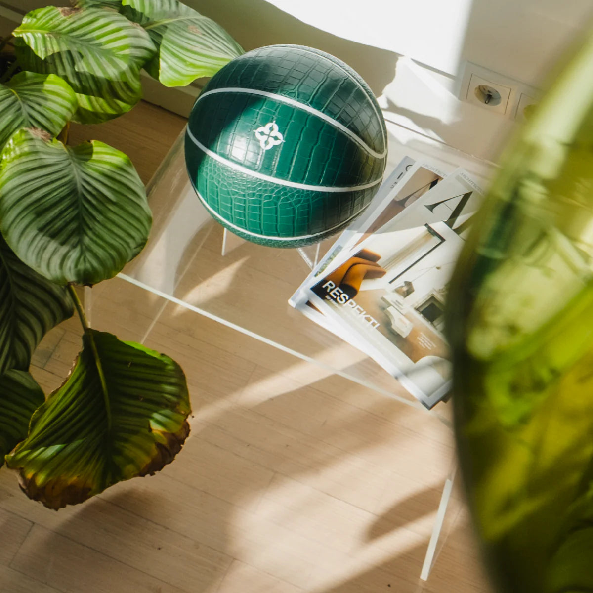 Palla da basket verde scuro con texture coccodrillo appoggiata su tavolino trasparente.