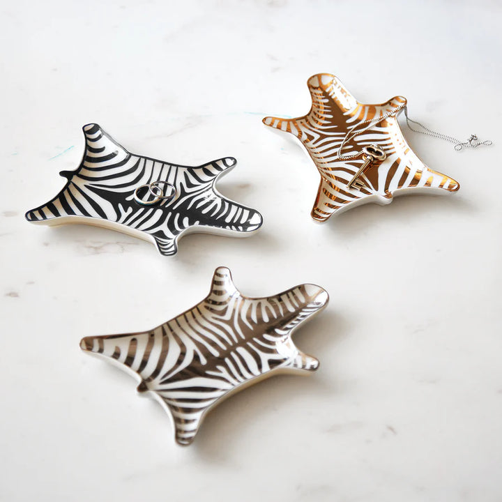 Tre portaoggetti a forma di pelle di zebra. Base bianca, strisce oro, argento e nero. Sfondo tavolo marmo