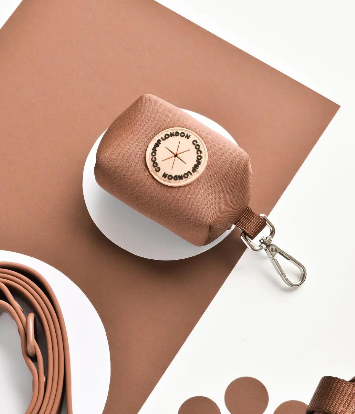 Porta sacchetti marrone con moschettone, marchio rotondo bianco con scritta Cocopup. 