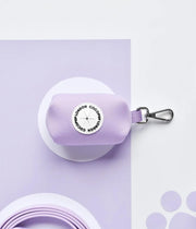 Porta sacchetti lilla con moschettone, marchio rotondo bianco con scritta Cocopup. Sfondo lilla