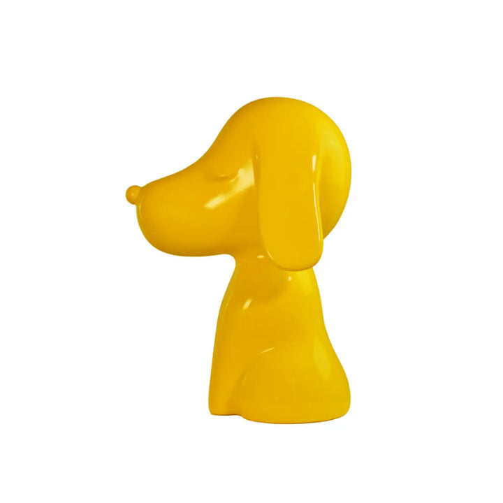 Profilo statua gialla a forma di cane, con occhi naso e bocca. Sfondo bianco