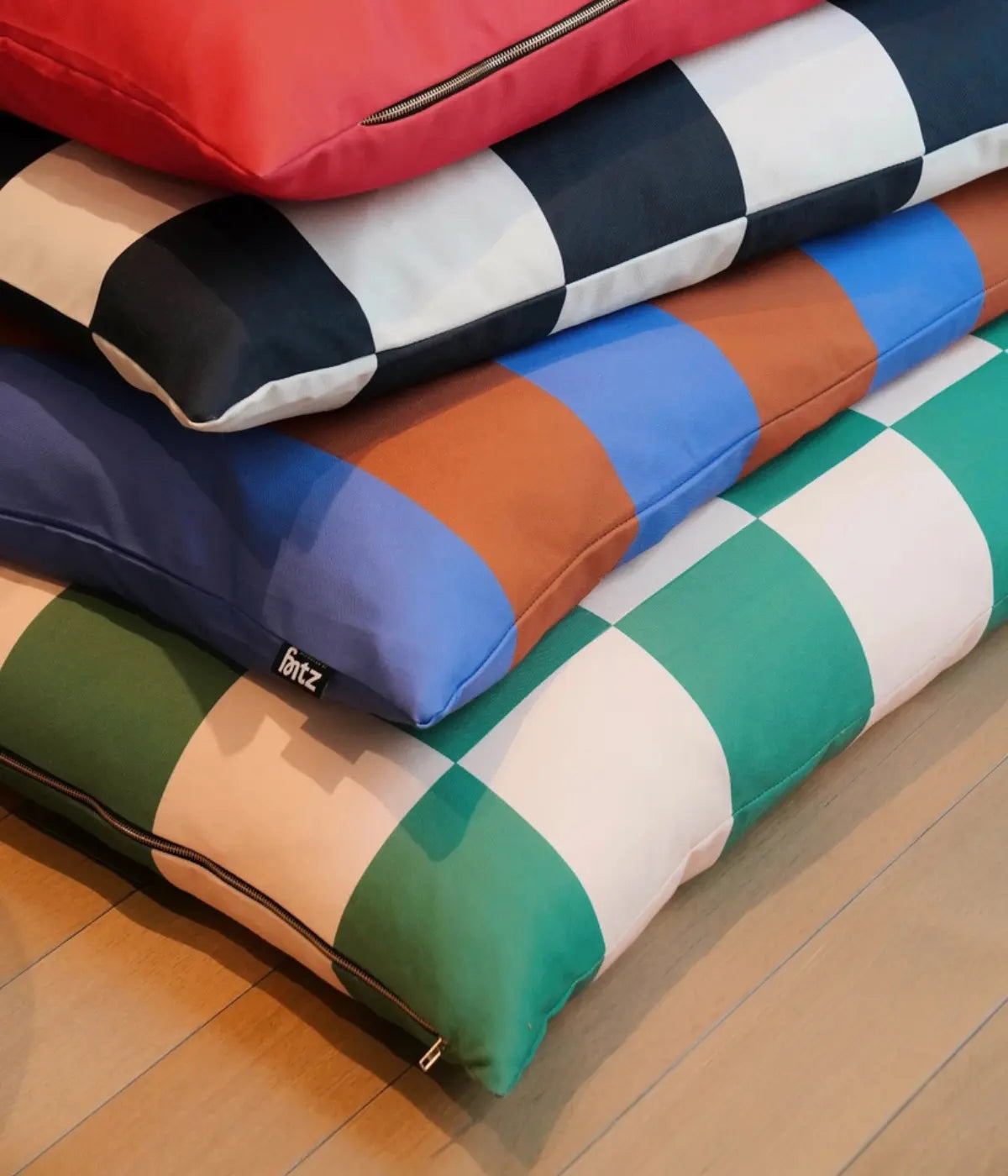Quattro cucce scacchi nero e bianco, verde e rosa, righe viola e marroni, rosso. Sfondo pavimento