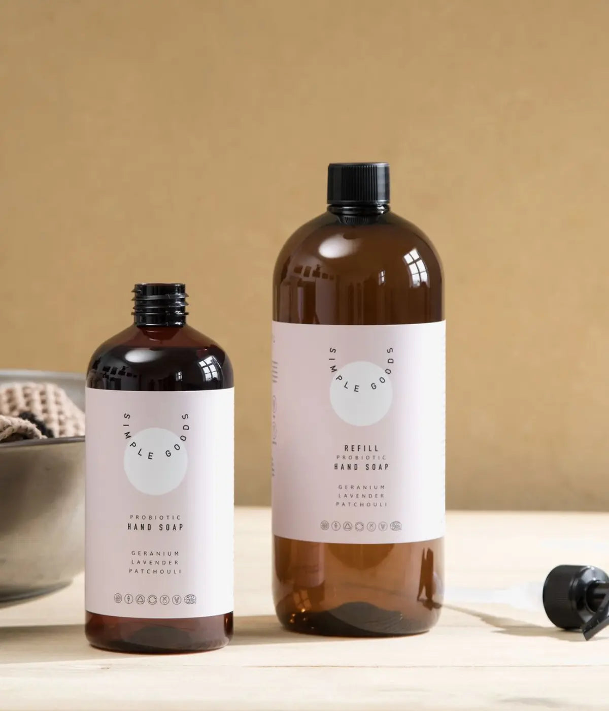 Due bottiglie marroni con etichetta rosa. Una refill, una distender sapone mani. Sfondo tavolo bianco