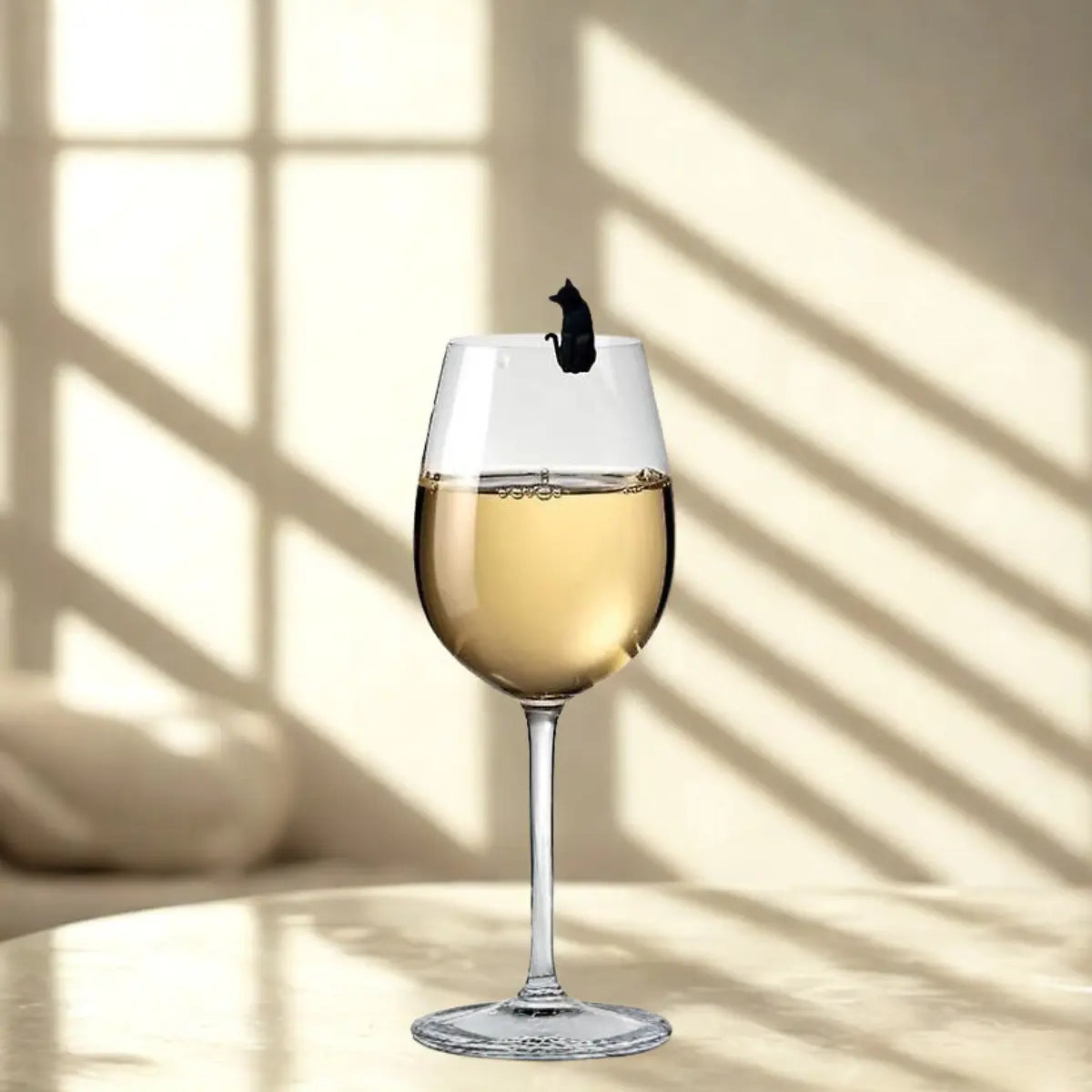 Calice di vino bianco con gatto nero come segnabicchiere. Sfondo tavolo bianco