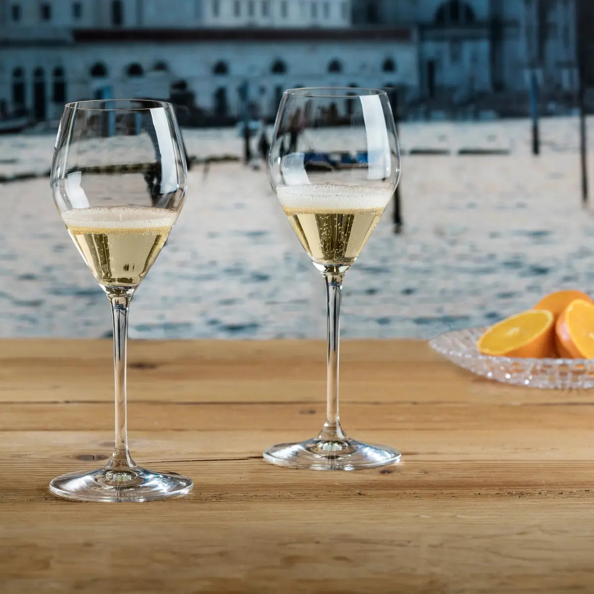 Due bicchieri di cristallo contenenti prosecco appoggiati su un tavolo di legno.