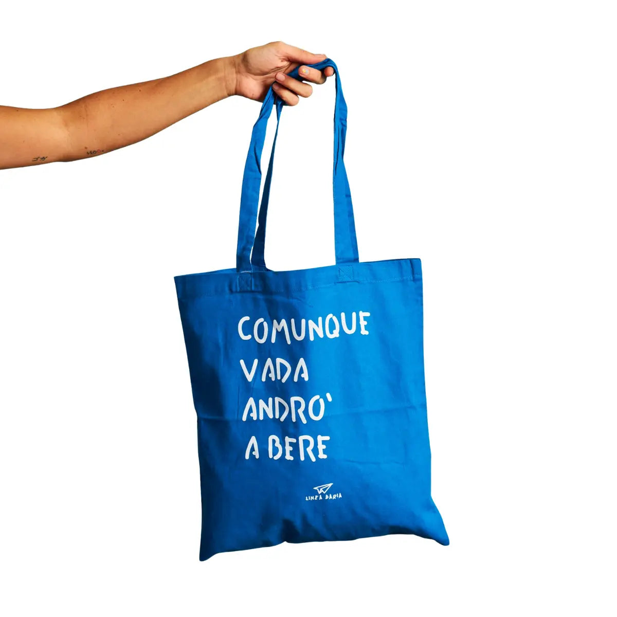 Una mano che tiene la shopper blu di Linea Daria con la scritta "Comunque vada andrò a bere"
