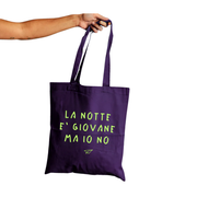 Una mano che tiene la shopper viola di Linea Daria con la scritta "La notte è giovane ma io no"