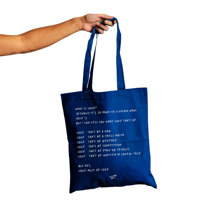 Una mano che tiene la shopper blu di Linea Daria con la scritta "What is love?"