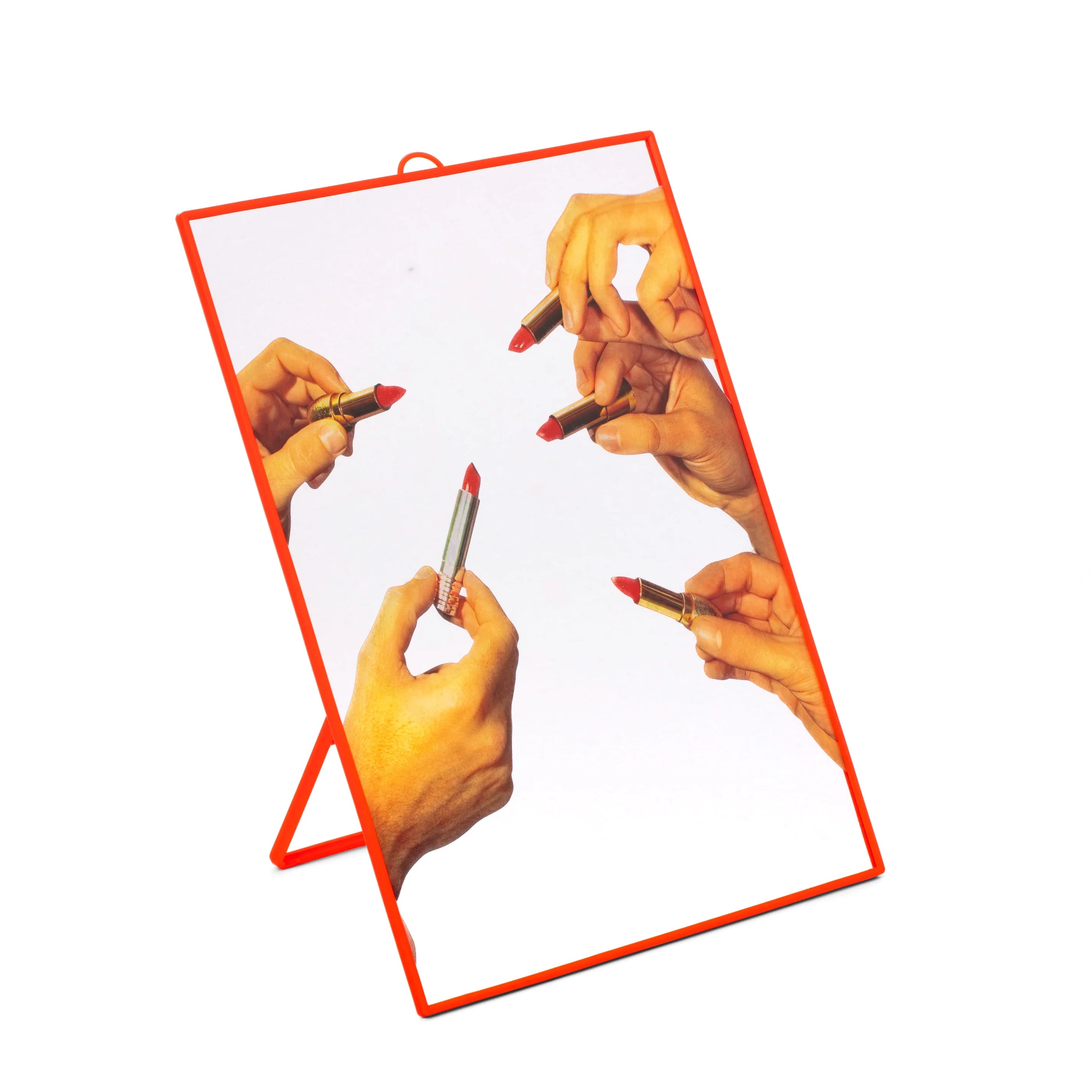 Specchio medio con grafica iconica di cinque mani che tengono rossetti. Cornice rossa di plastica con supporto. Sfondo bianco 
