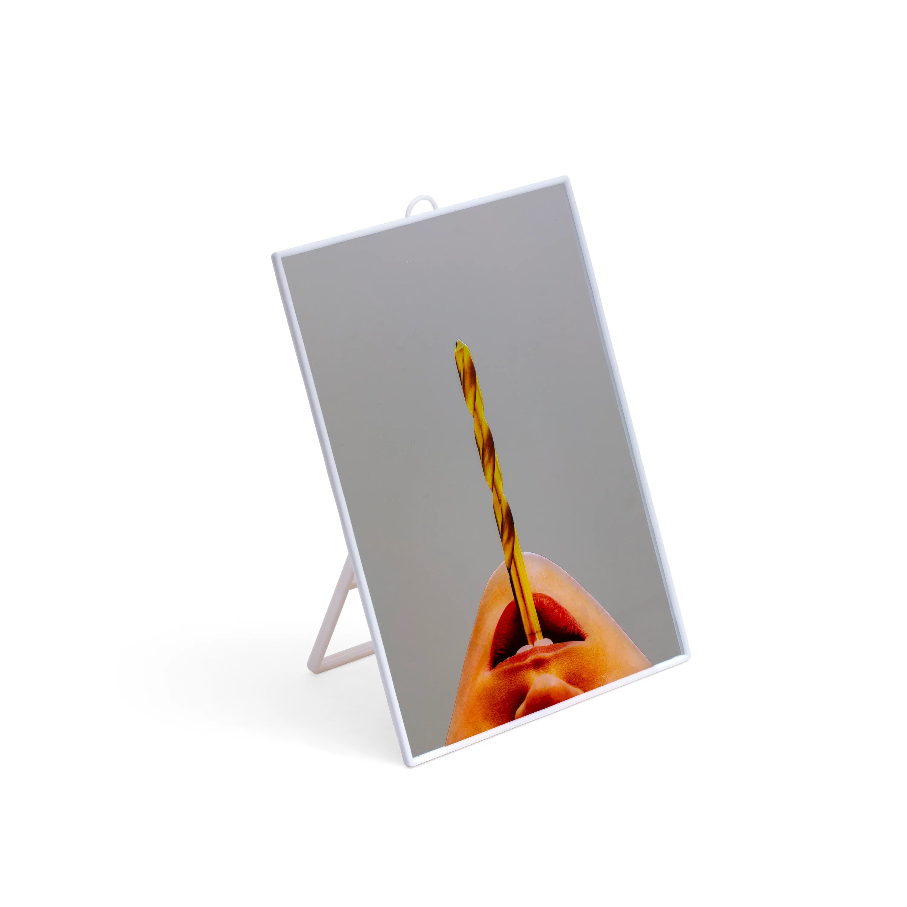 Vista laterale dello specchio Drilll della collezione Toiletpaper di Seletti rappresentante una bocca femminile che tiene tra le labbra una punta di trapano. La cornice e il supporto dello specchio sono in plastica bianca 