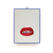 Specchio con grafica "Shit" di Toiletpaper x Seletti. Lo specchio è incorniciato in una cornice di plastica blu e la grafica con le labbra rosse e la scritta shit è posizionata nella parte inferiore dello specchio. Sfondo bianco