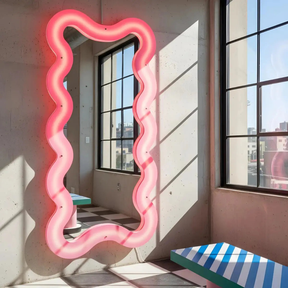 Specchio supercurve di Seletti realizzato in plexiglass rosa. Retroilluminato e dalle forme sinuose e morbide. Appeso su un muro di cemento in una casa