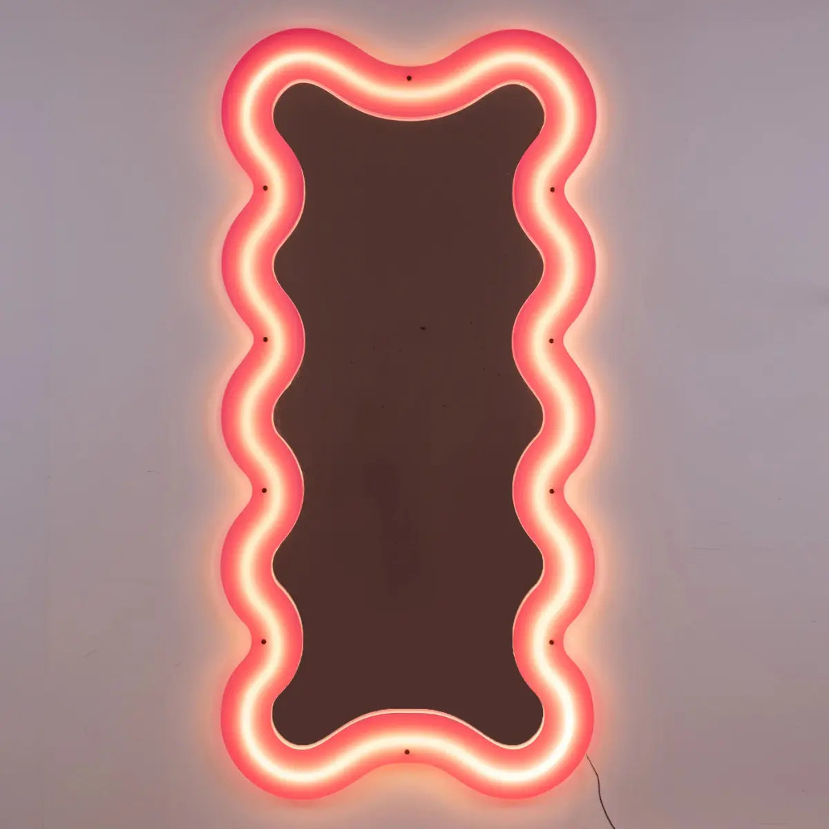Specchio supercurve di Seletti realizzato in plexiglass rosa. Retroilluminato e dalle forme sinuose e morbide.