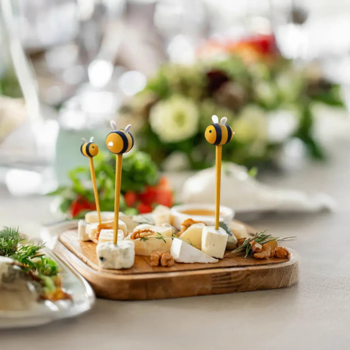 Stecchini decorativi con ape in cima inseriti in dei pezzi di formaggio su un tagliere