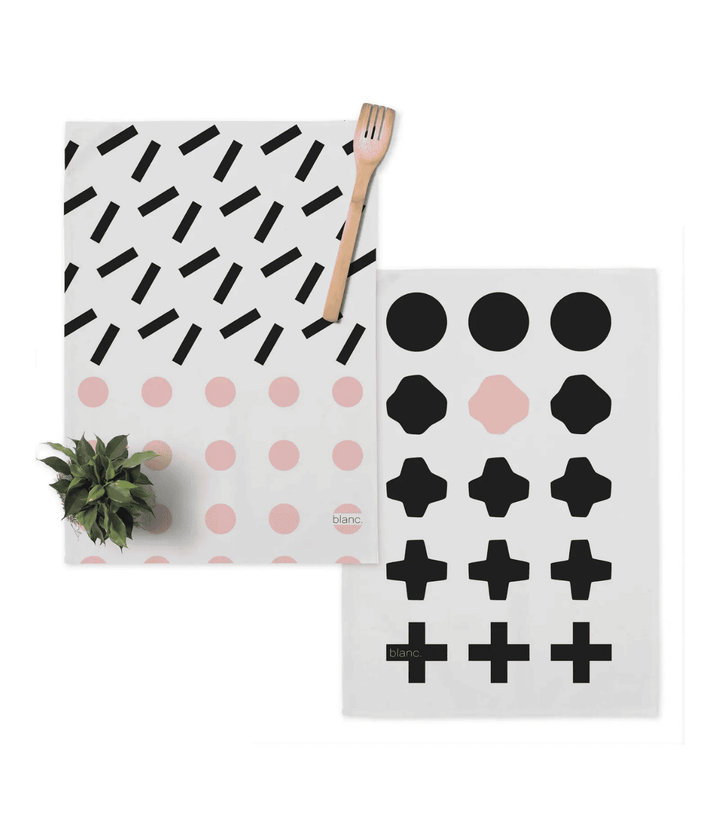 Due strofinacci con decorazioni nere e rosa. Con forchetta di legno e piantina verde. Sfondo bianco.