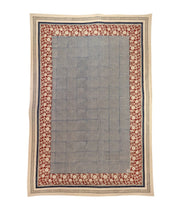 Tovaglia rettangolare in cotone con pattern fine a quadretti neri e bianchi, circondato da una larga bordura rossa e beige decorata con motivi floreali intricati.