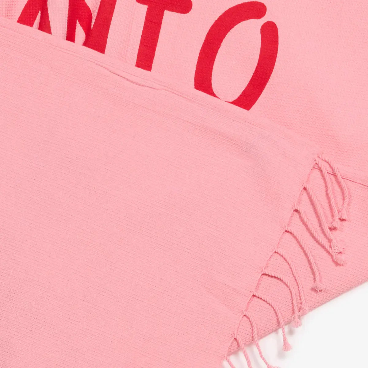 Dettaglio del telo mare con scritta rossa e sfondo rosa. Frange nella parte inferiore.