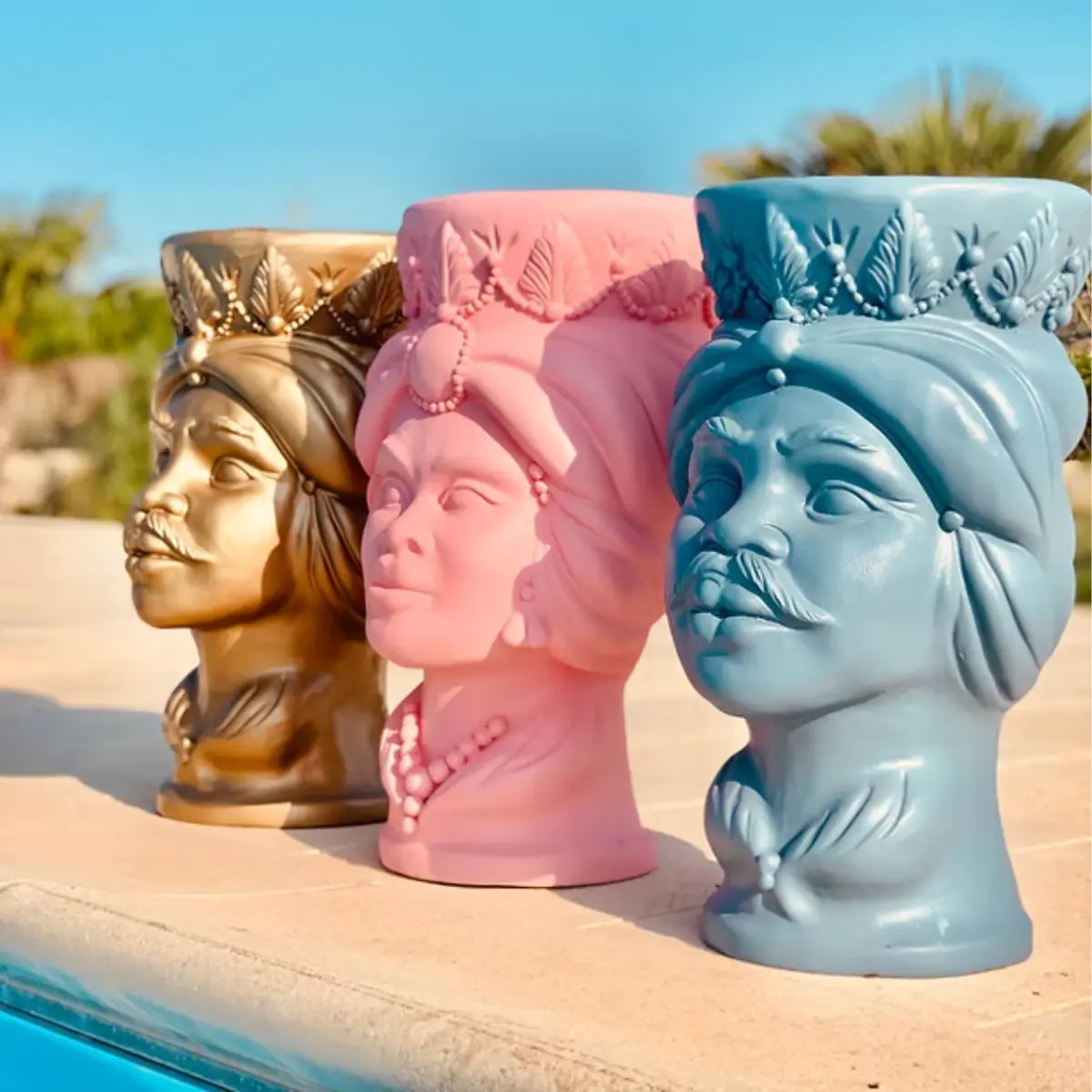 Dettaglio di tre teste di moro color celeste, rosa e oro, posizionate a bordo piscina