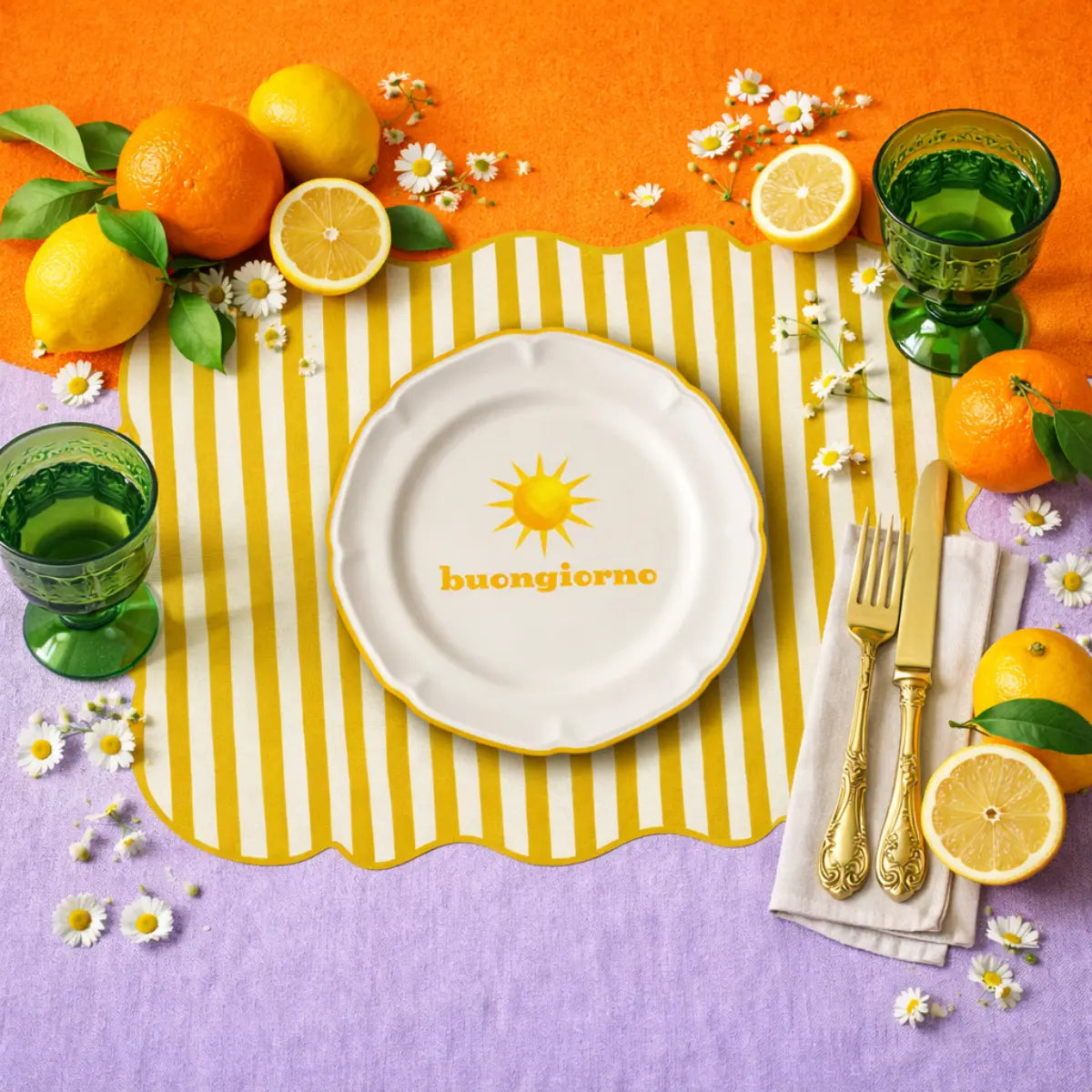 Tovaglietta dalla forma irregolare a righe bianche e gialle con al centro un disegno di un piatto bianco con la scritta "buongiorno" e un sole giallo disegnato. La tovaglietta è appoggiata su un tavolo cona altri oggetti