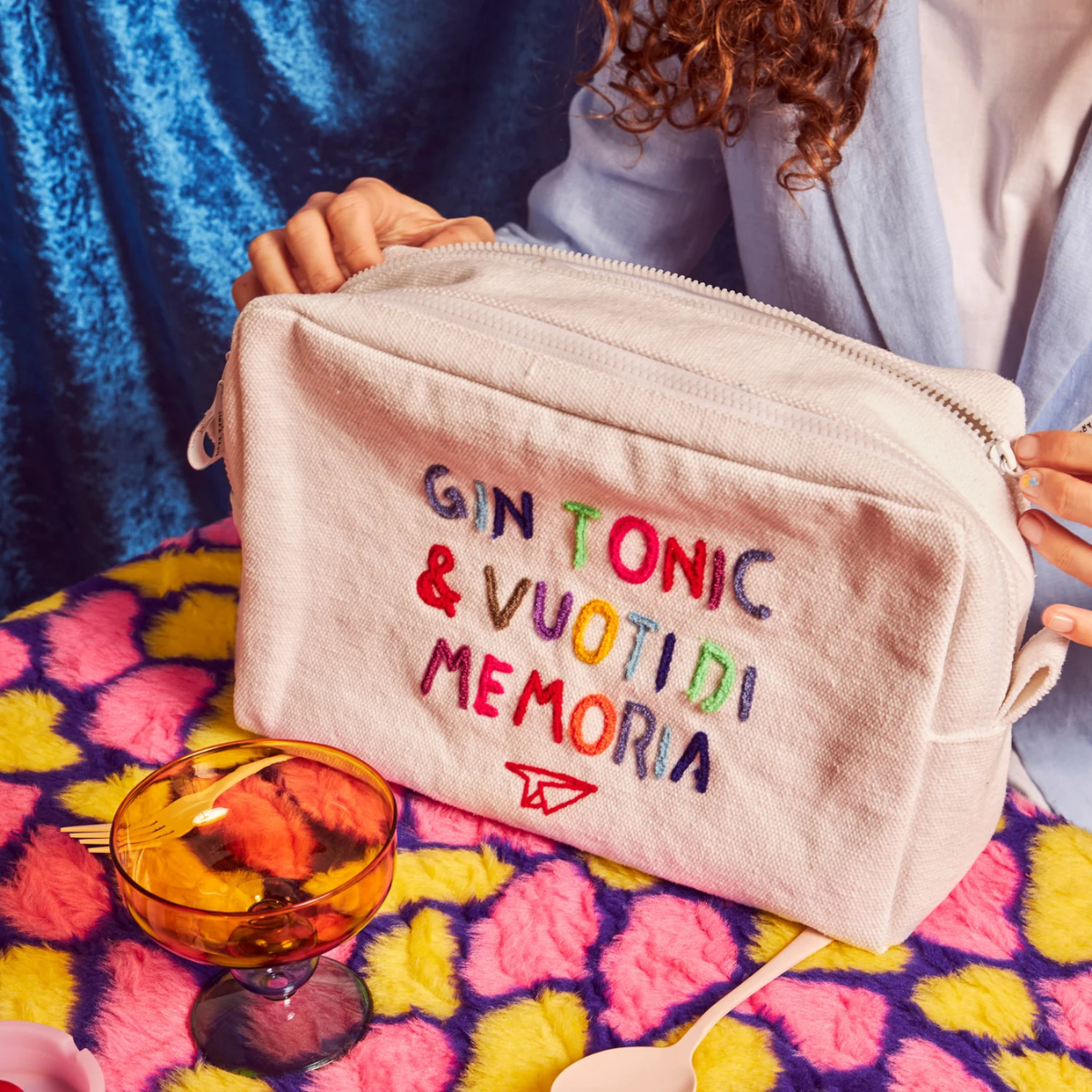 Mani che utilizzano la trousse di Linea Daria nella versione bianca grande con la scritta multicolore "Gin Tonic e vuoti di memoria"