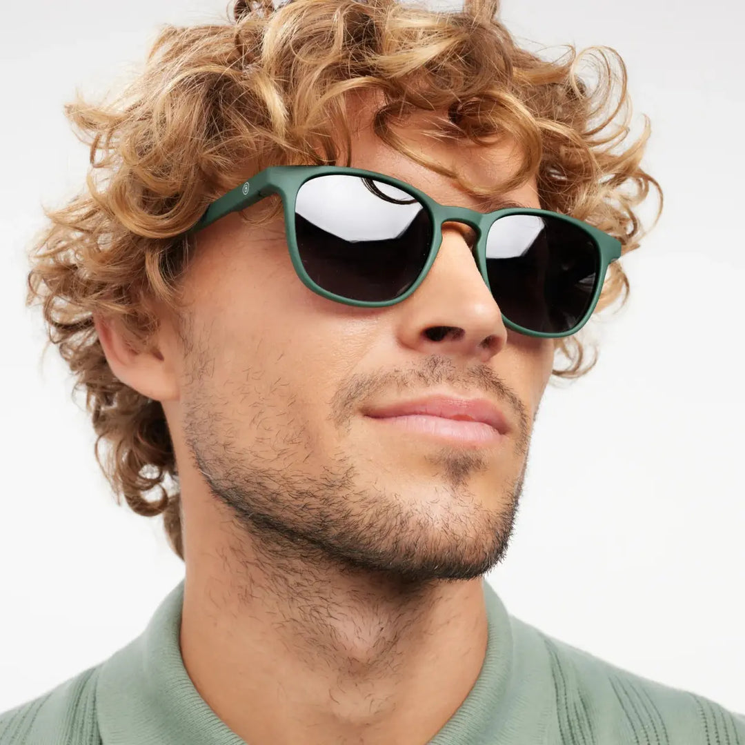 Occhiale da sole finitura verde opaca, con  indossato da uomo riccio biondo.
