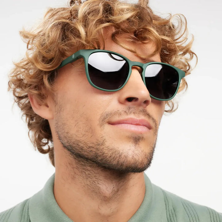 Occhiale da sole finitura verde opaca, con  indossato da uomo riccio biondo.
