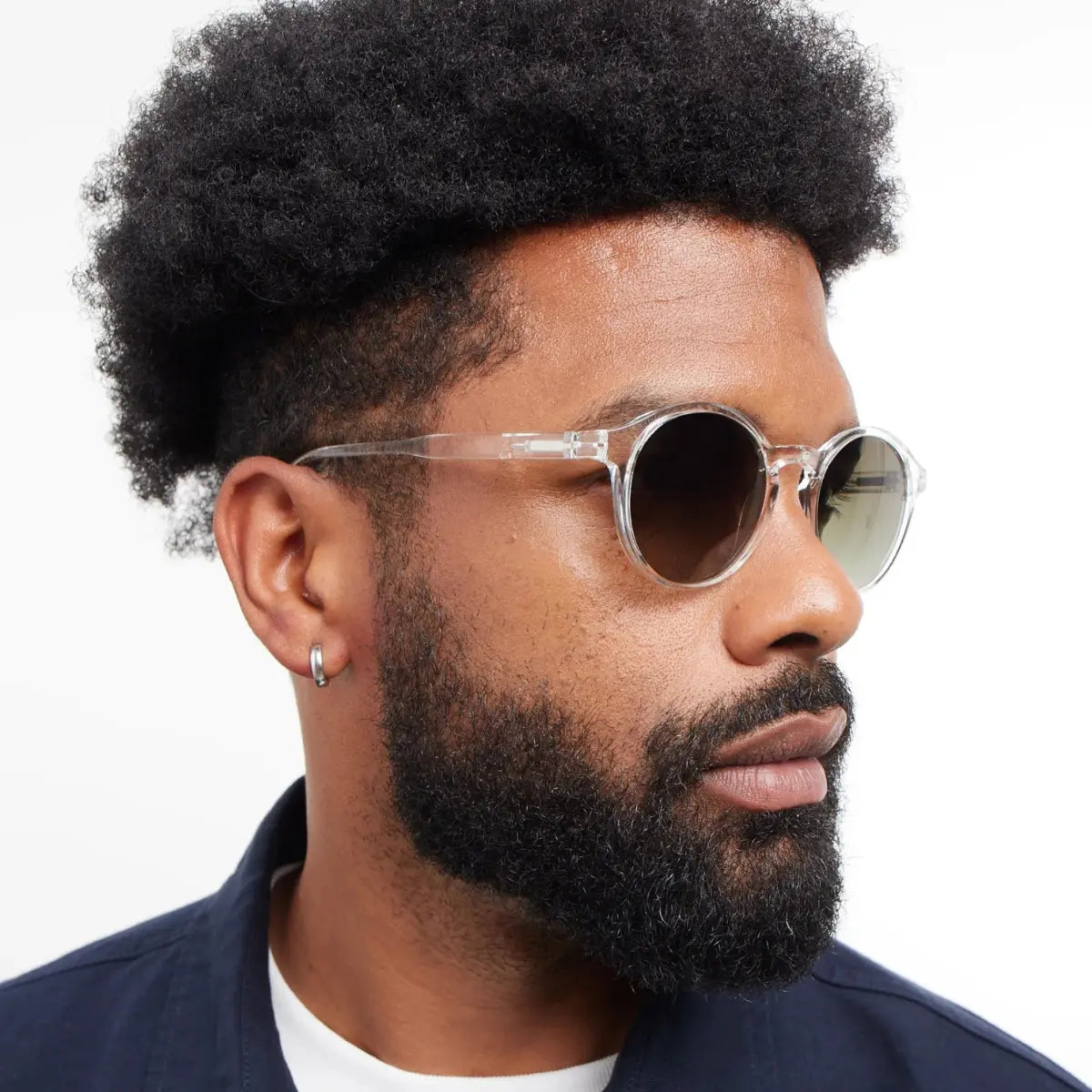 Occhiale da sole finitura trasparente lucida, con lenti scure indossato da uomo moro riccio.
