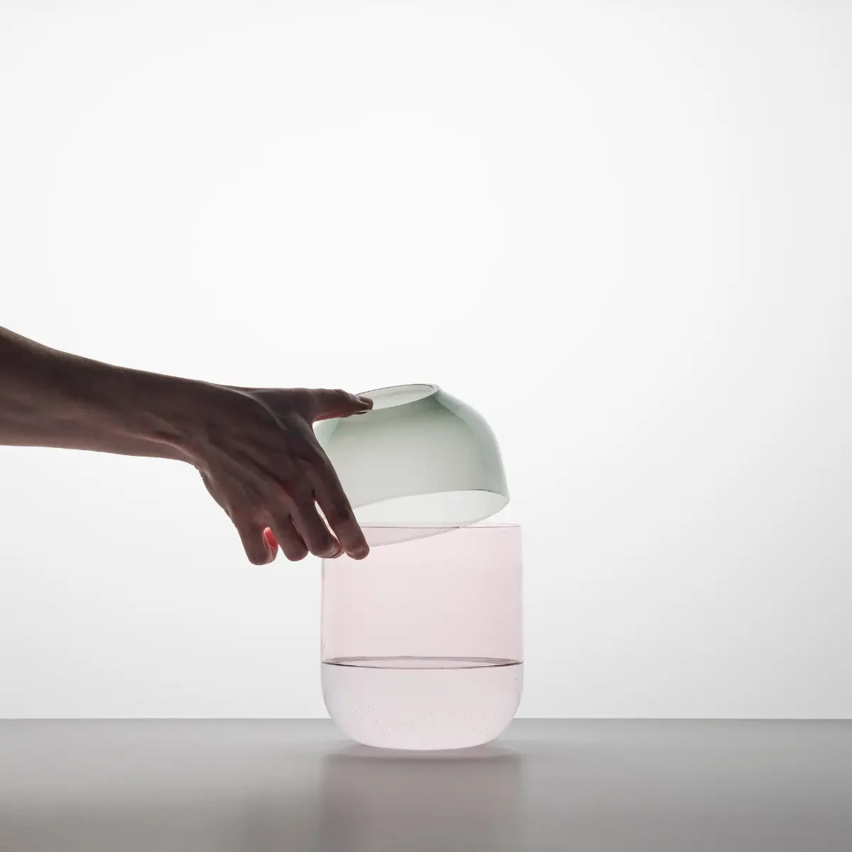 Una mano che tiene il coperchio del vaso fio nella versione grigio con base rosa
