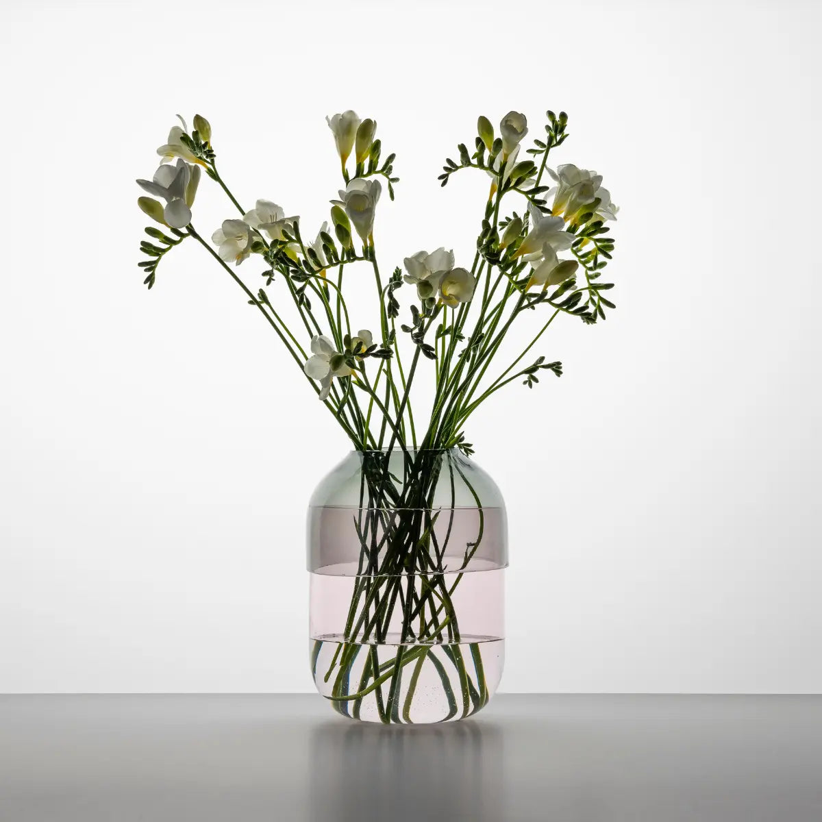 Vaso Fio con base rosa e coperchio grigio smoke con dei fiori all'interno. luce soffusa.
