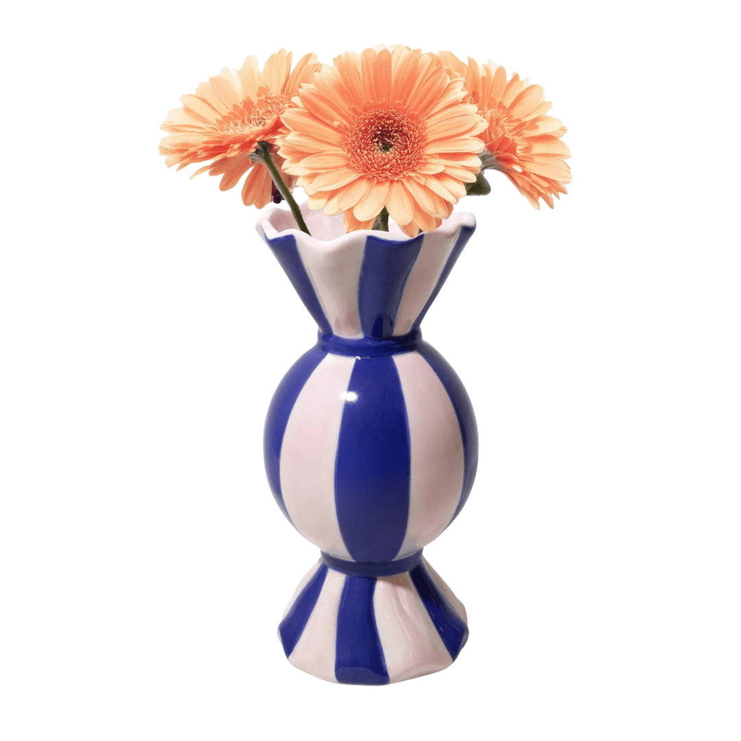 Vaso funfair a forma di caramella blu con fiori rosa inseriti su sfondo bianco.