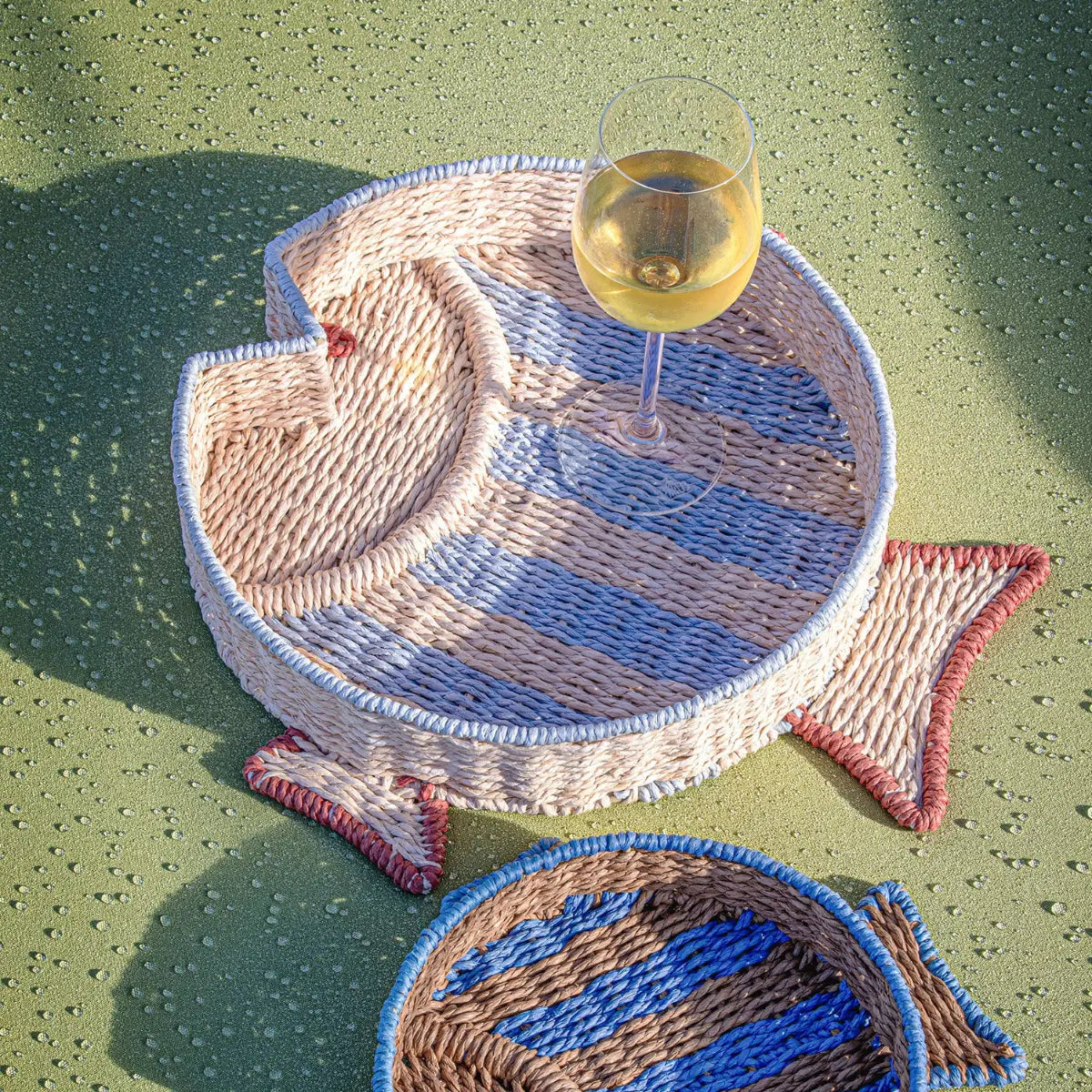 Vassoi a forma di pesce realizzato in carta intrecciata. Calice di vino e sfondo verde con gocce d'acqua 