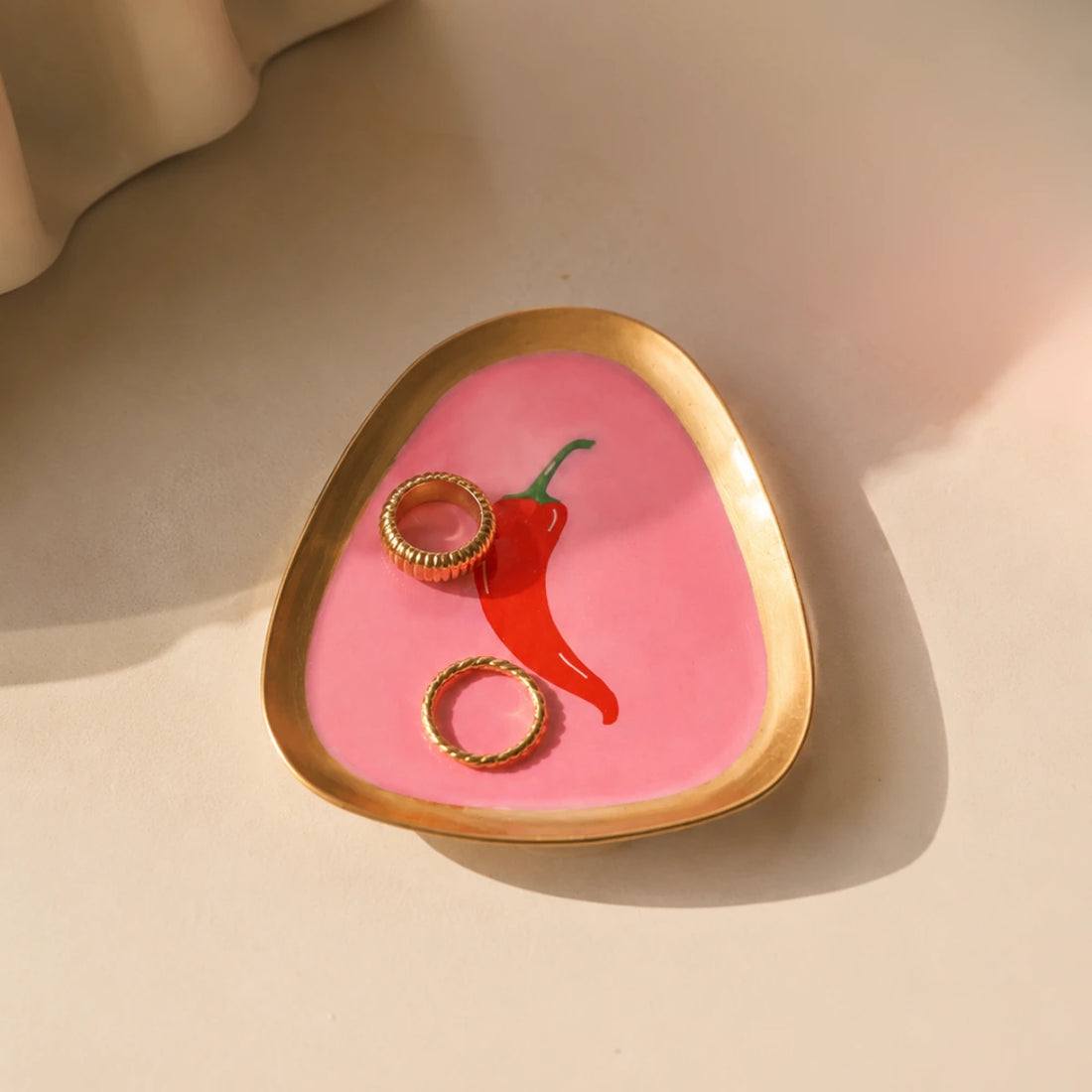 Vassoio Svuotatasche con forma irregolare e bordo dorato con peperoncino rappresentato al centro con sfondo fucsia.
