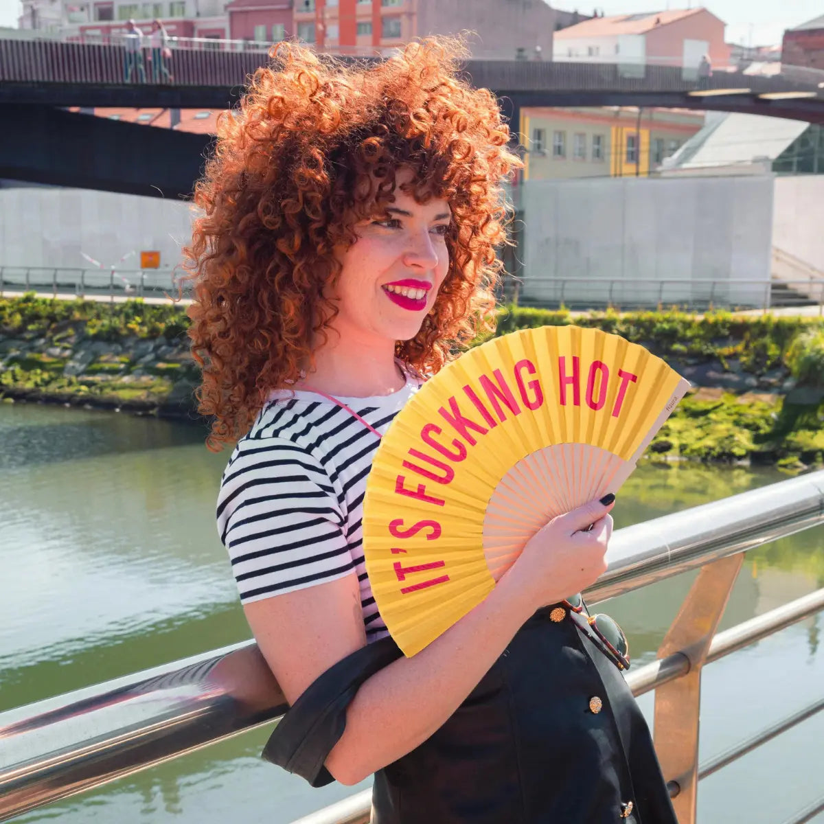 Donna che tiene in mano il ventaglio con scritta "It's fucking hot" con sfondo giallo e scritta fucsia.