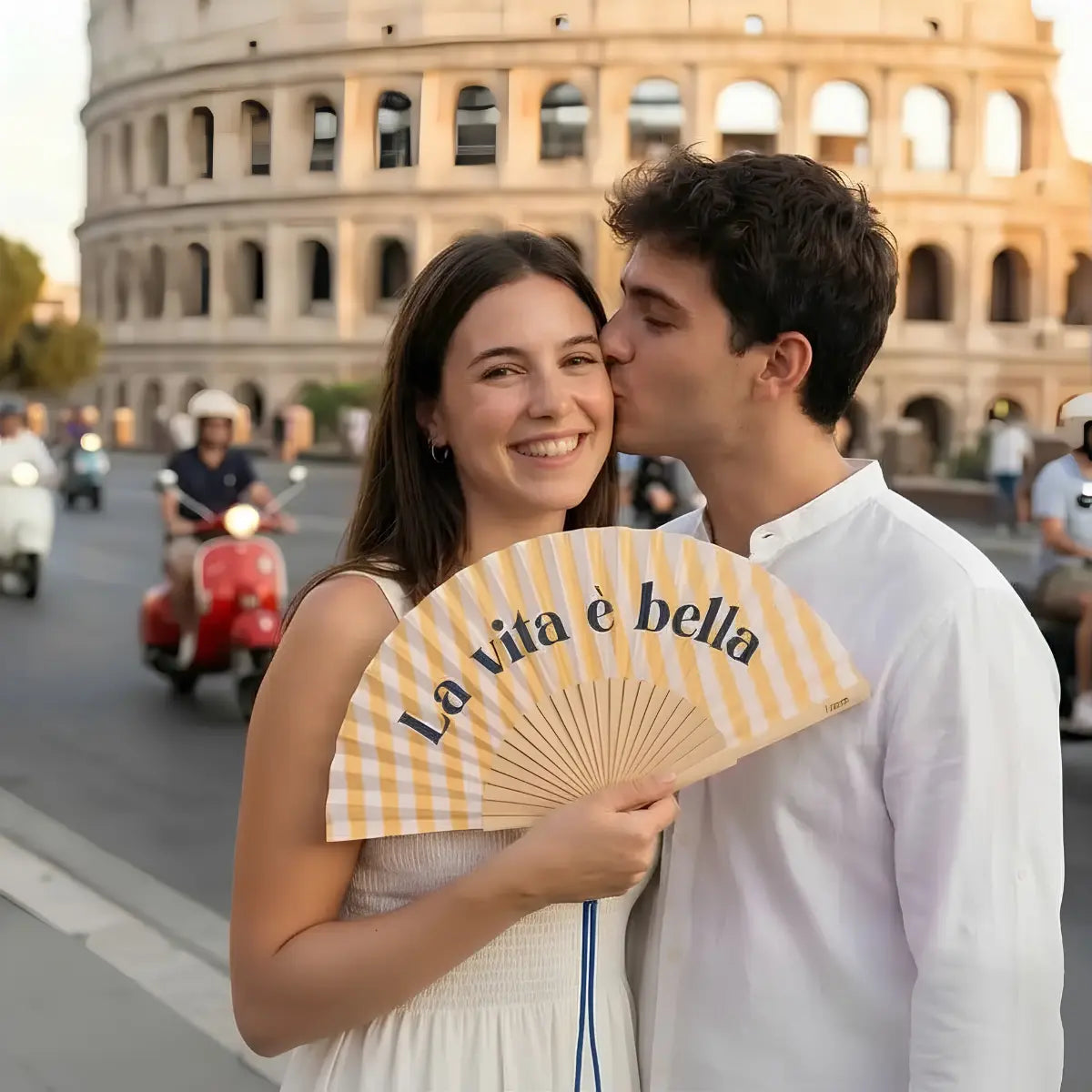 Due ragazzi con ventaglio con base a righe gialle e bianche e scritta blu "La vita è bella". 