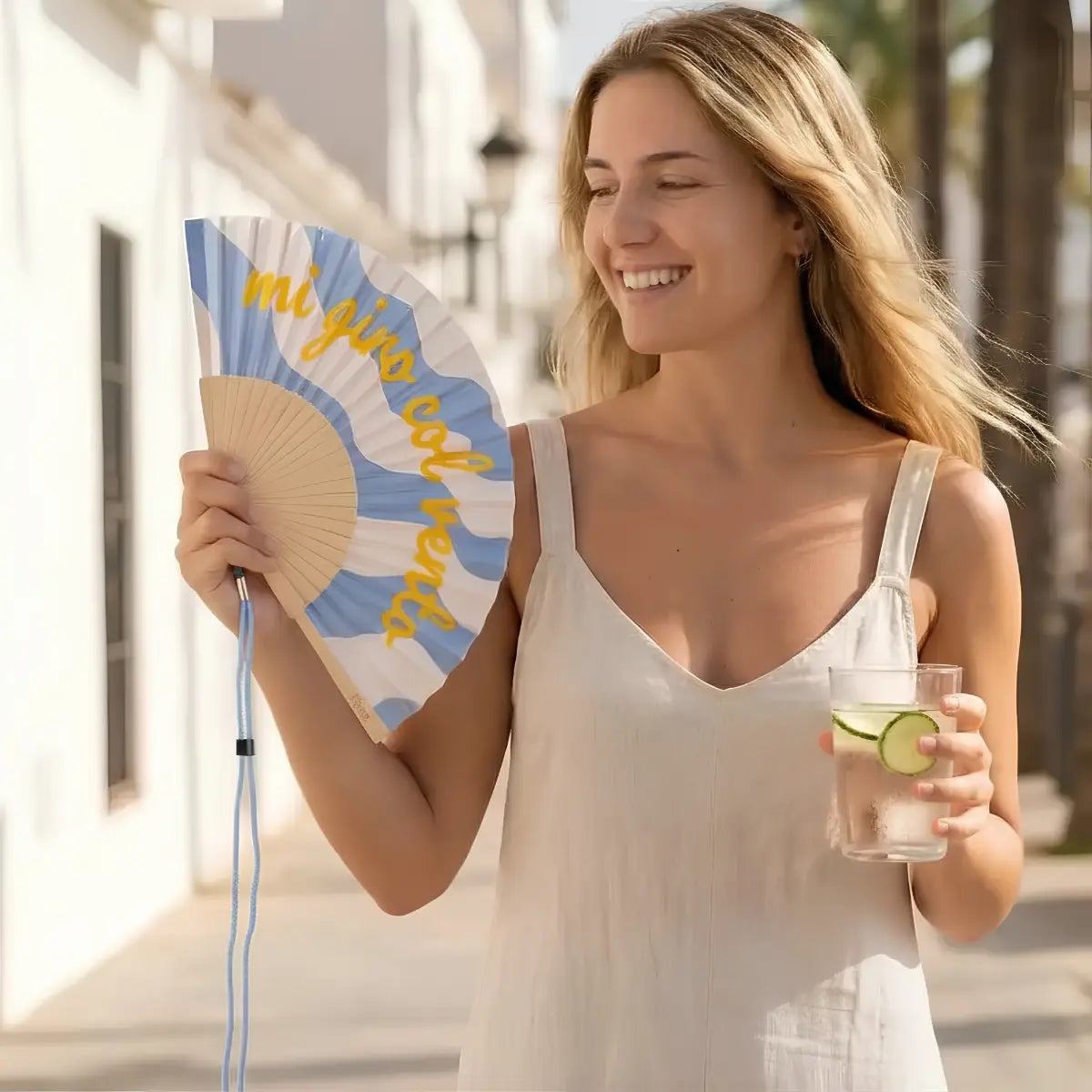 Donna con il ventaglio con sfondo fantasia azzurra e bianca con scritta gialla "Mi giro col vento"