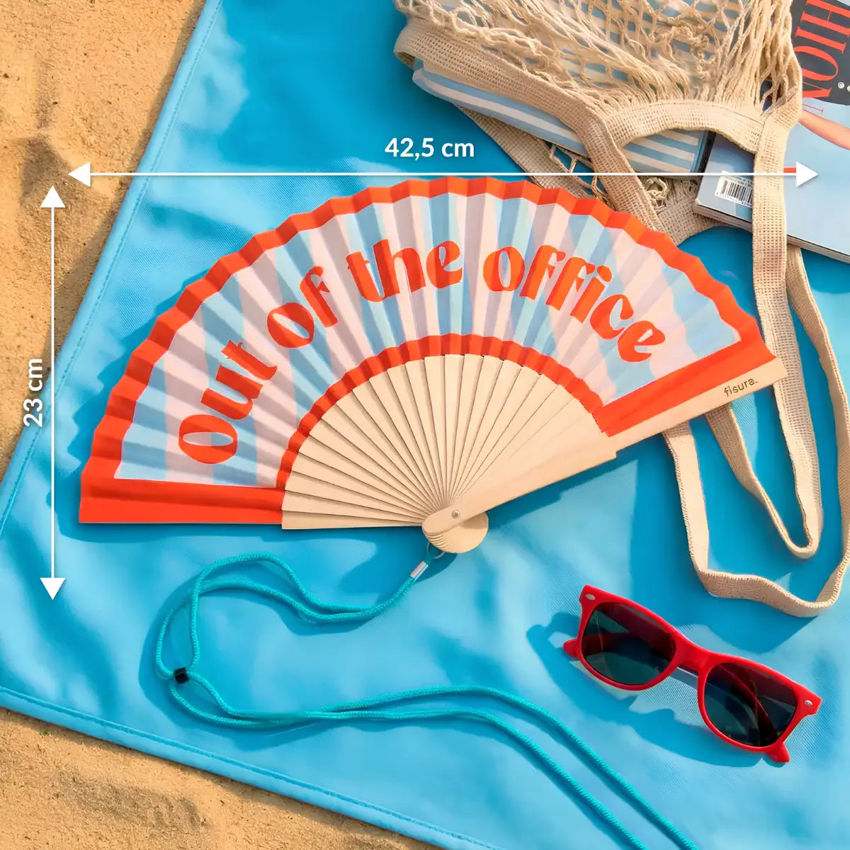 Ventaglio con sfondo a righe e scritta rossa "out of the office" appoggiato su un telo mare in spiaggia. Le misure del ventaglio sono segnate in bianco con delle frecce