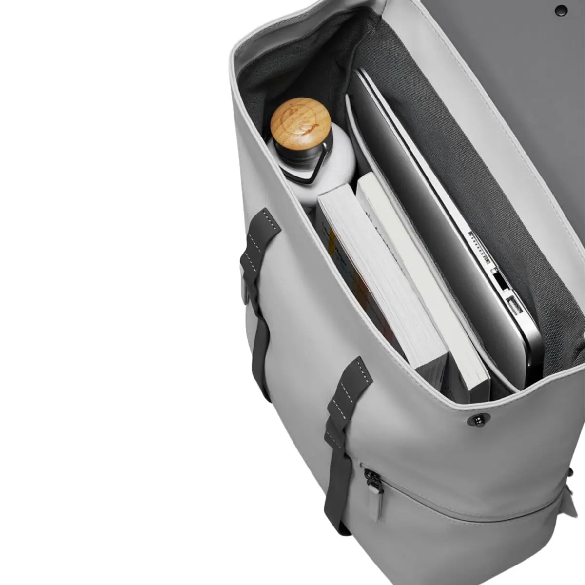 Vista dall'alto dell'interno dello zaino con patta. Computer nel comparto specifico, borraccia e libri nel comparto principale. Sfondo bianco