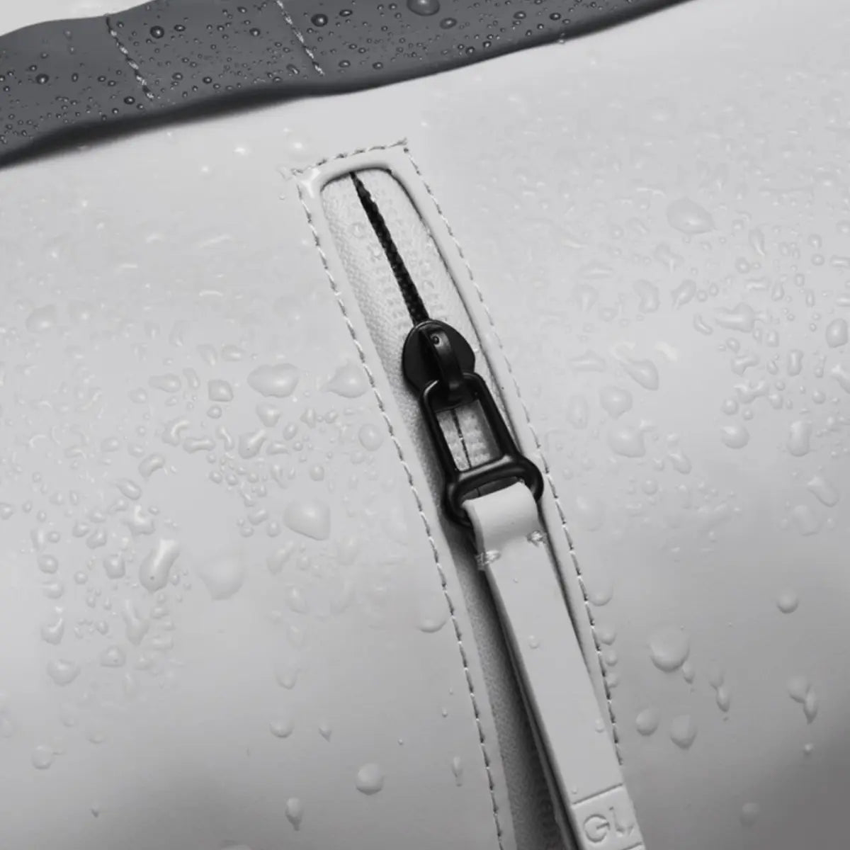 Dettaglio del materiale impermeabile dello zaino con patta. Gocce di acqua che bagnano il materiale e la zip. 