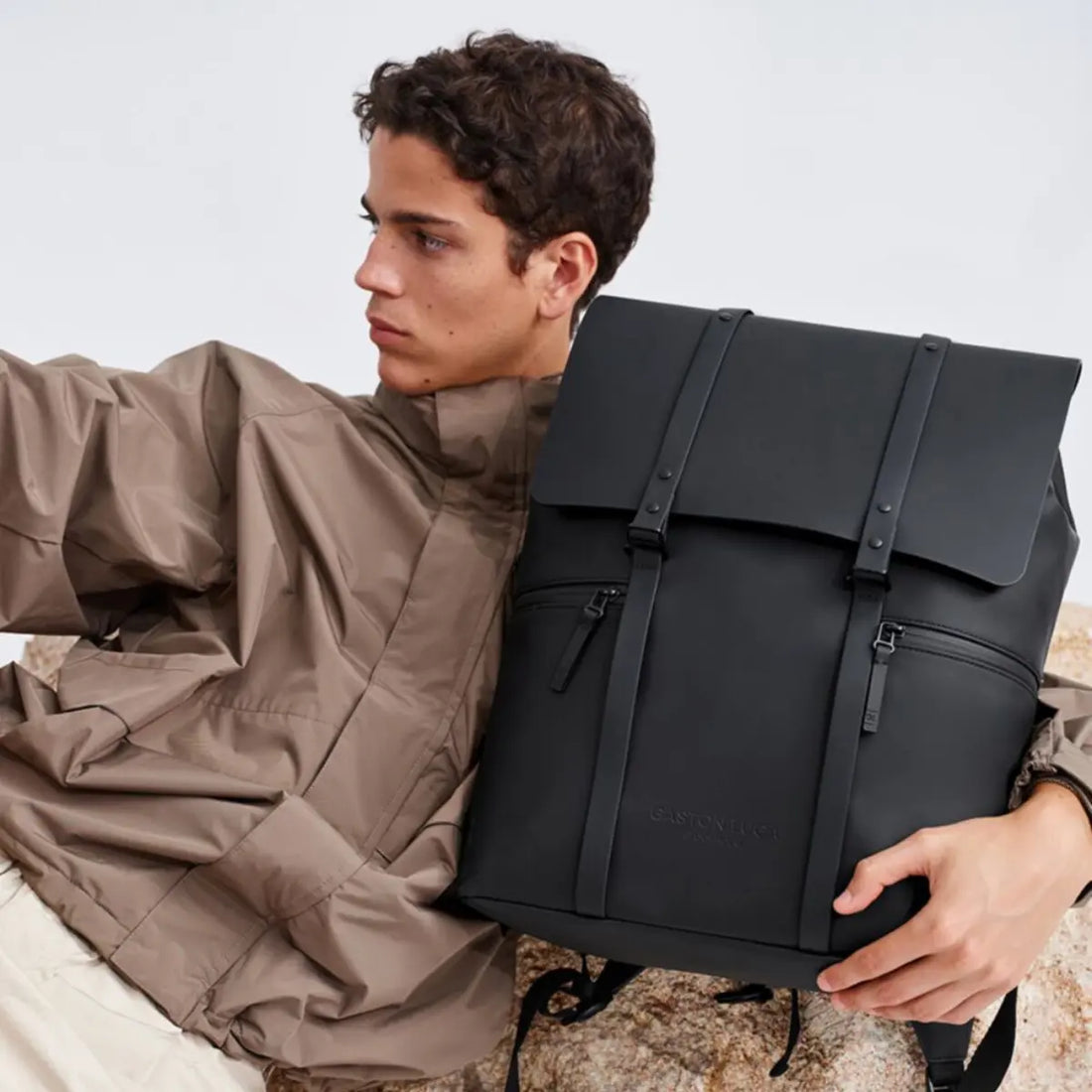 Ragazzo che tiene in mano lo zaino con patta 16''. Appoggiato ad una roccia