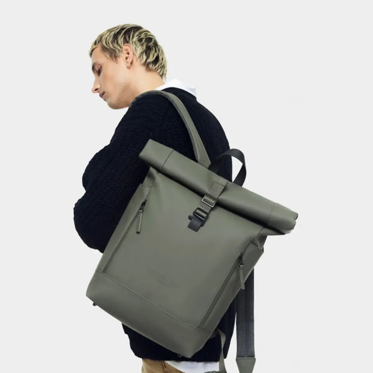 Ragazzo biondo che tiene sulla spalla lo zaino rolltop nella versione verde. Sfondo bianco