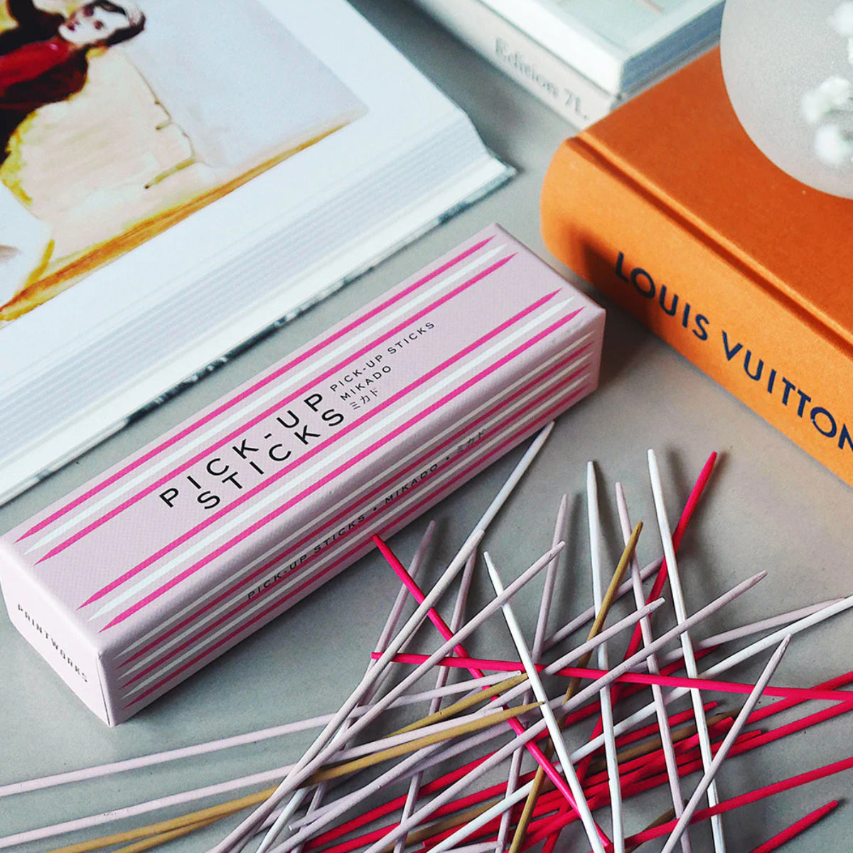 Scatola rosa e bastoncini di diversi colori su tavolo grigio, libri adiacenti