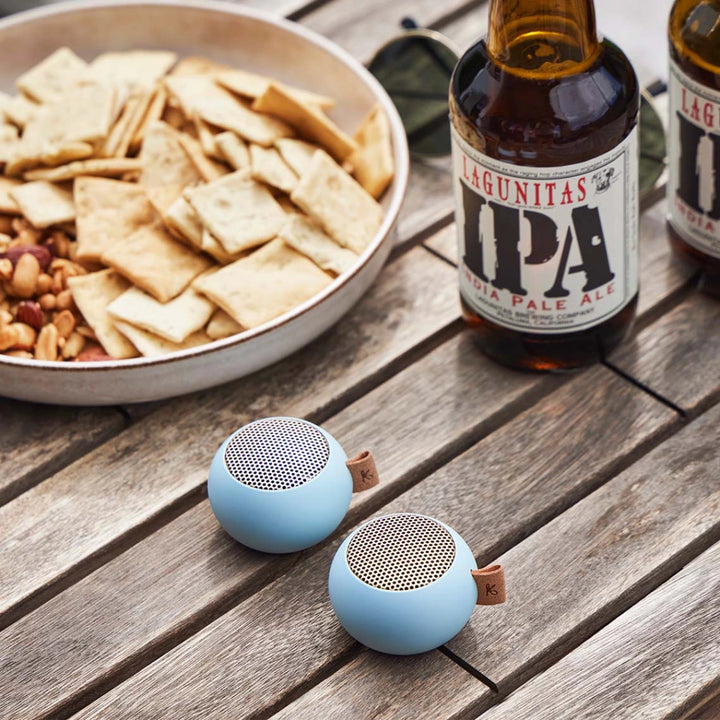 due mini casse audio portatili azzurre, su tavolo legno. Birre e snack.