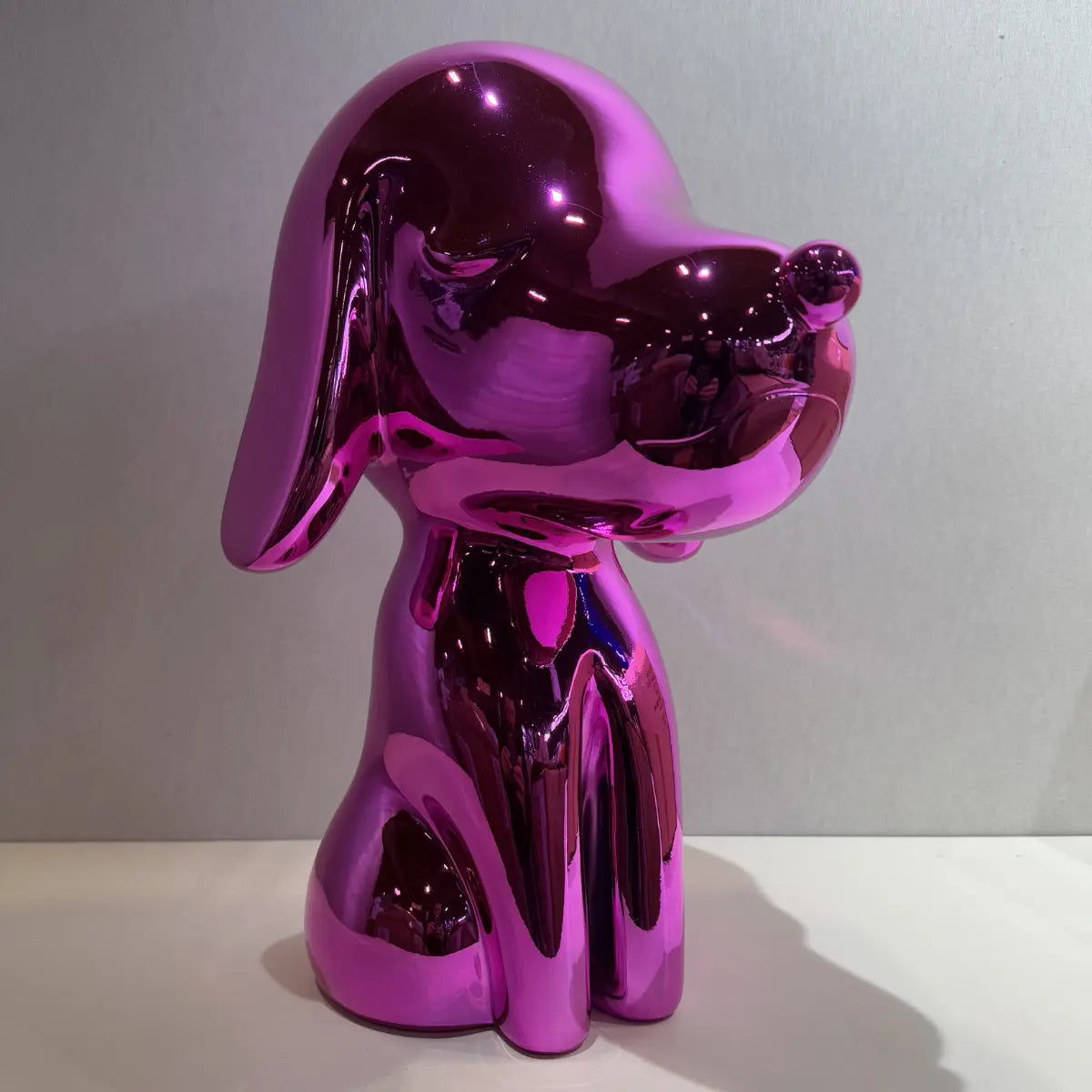 Statua Arturo fuxia appoggiata su mensola grigia. Sfondo grigio