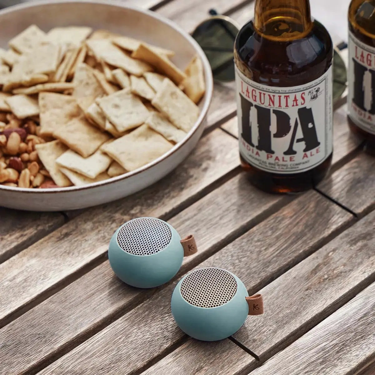 due mini casse audio portatili azzurre, su tavolo legno. Birre e snack.